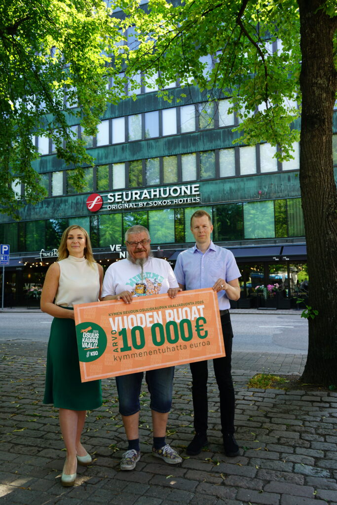 Arvontavoittaja ja palkinnon luovuttajat puistokadulla Kotkan Seurahuoneen edessä.